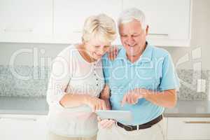 Senior couple laughing using tablet in kitchen