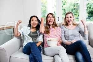 Young female friends cheering while sitting on sofa