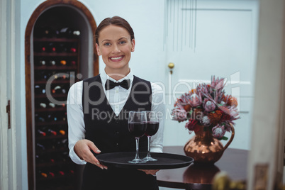 Smiling waitress holding a tray with glasses of red wine