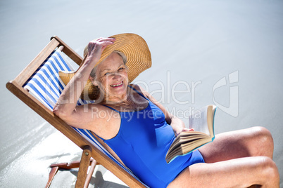 Pretty mature woman reading a book lying on deck chair