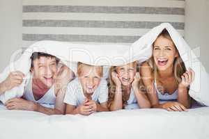 Portrait of family covered with duvet on bed