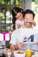 Happy daughter covering father eyes while holding gift box