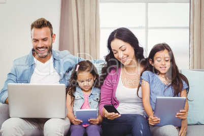 Family using modern technologies while sitting on sofa
