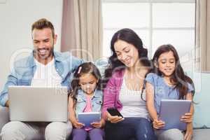 Family using modern technologies while sitting on sofa