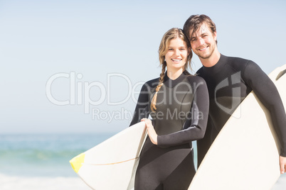 Portrait of couple with surfboard standing on the beach