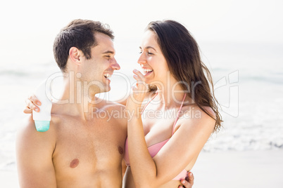 Happy woman applying moisturizer on mans nose