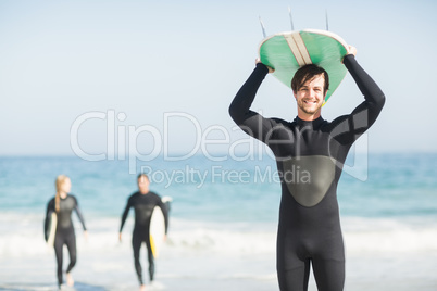 Happy man in wetsuit carrying surfboard over head