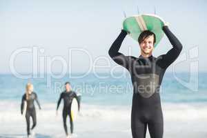 Happy man in wetsuit carrying surfboard over head