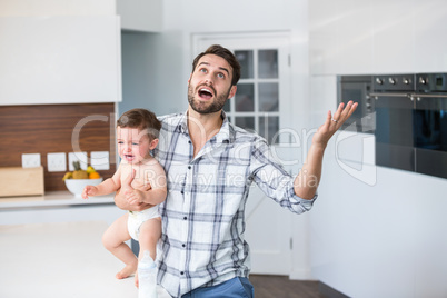 Frustrated father holding crying baby boy in kitchen