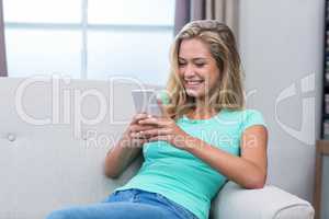 Young woman smiling while using mobile phone on sofa