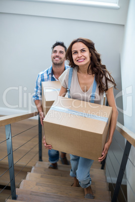 Smiling couple holding cardboard boxes while climbing steps