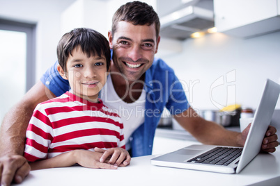 Portrait of father and son using laptop in kitchen