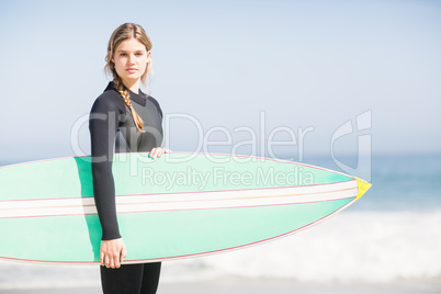 Portrait of woman in wetsuit holding a surfboard on the beach