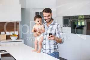 Father using mobile phone while holding baby boy