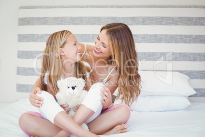 Smiling mother and daughter sitting on bed