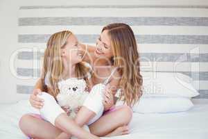 Smiling mother and daughter sitting on bed