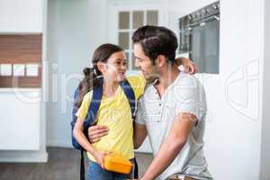 Father talking to smiling daughter holding lunch box