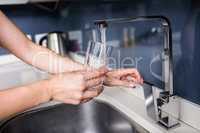 Woman filling water in glass at kitchen sink