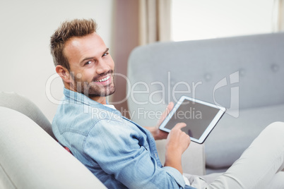 Young man smiling while using digital tablet on sofa