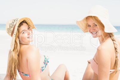 Pretty women in bikini and beach hat sitting on the beach