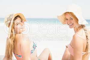 Pretty women in bikini and beach hat sitting on the beach