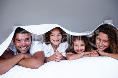 Portrait of happy family lying under a bedsheet