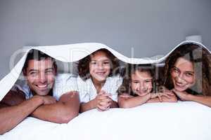 Portrait of happy family lying under a bedsheet