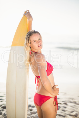 Woman in bikini standing with a surfboard on the beach