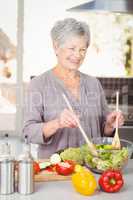 Happy senior woman tossing salad while standing in kitchen