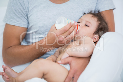 Man feeding milk to baby girl at home