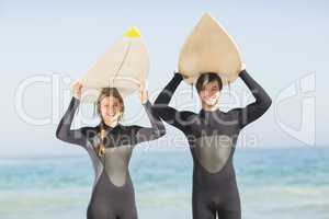 Portrait of couple in wetsuit carrying surfboard over head