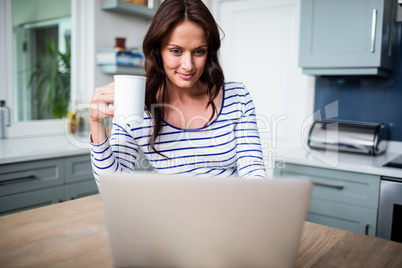 Smiling woman working on laptop while holding coffee mug