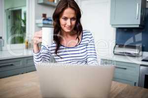 Smiling woman working on laptop while holding coffee mug