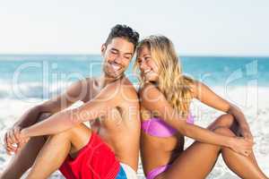 Happy couple sitting back to back on beach