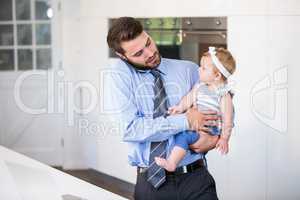 Businessman talking on cellphone while carrying daughter