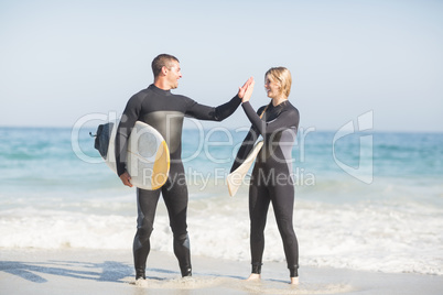 Couple holding a surfboard and giving a high five to each other