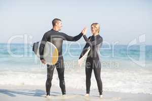 Couple holding a surfboard and giving a high five to each other