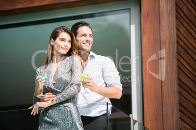 Couple with drinks standing in balcony at resort