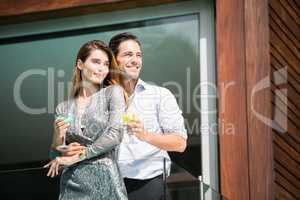 Couple with drinks standing in balcony at resort