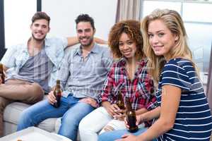 Happy multi-ethnic friends holding beer while sitting on sofa