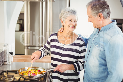 Happy senior man looking at wife cooking food
