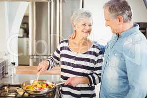 Happy senior man looking at wife cooking food