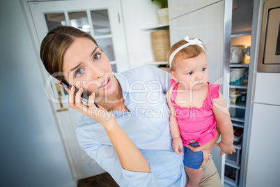 Tensed woman talking on mobile phone while carrying baby girl