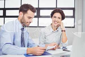 Businessman working while happy female colleague sitting beside