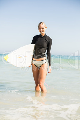 Woman in wetsuit holding a surfboard on the beach