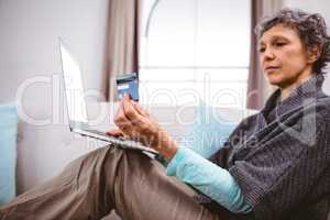 Woman looking at credit card while using laptop