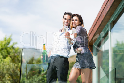 Cheerful couple showing champagne glass at balcony