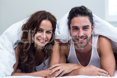Portrait of smiling couple lying under blanket