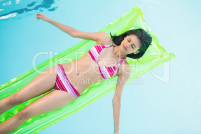 Beautiful woman in bikini lying on air bed in swimming pool