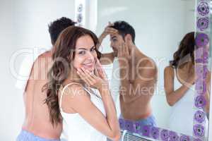 Young woman standing by husband in front of mirror